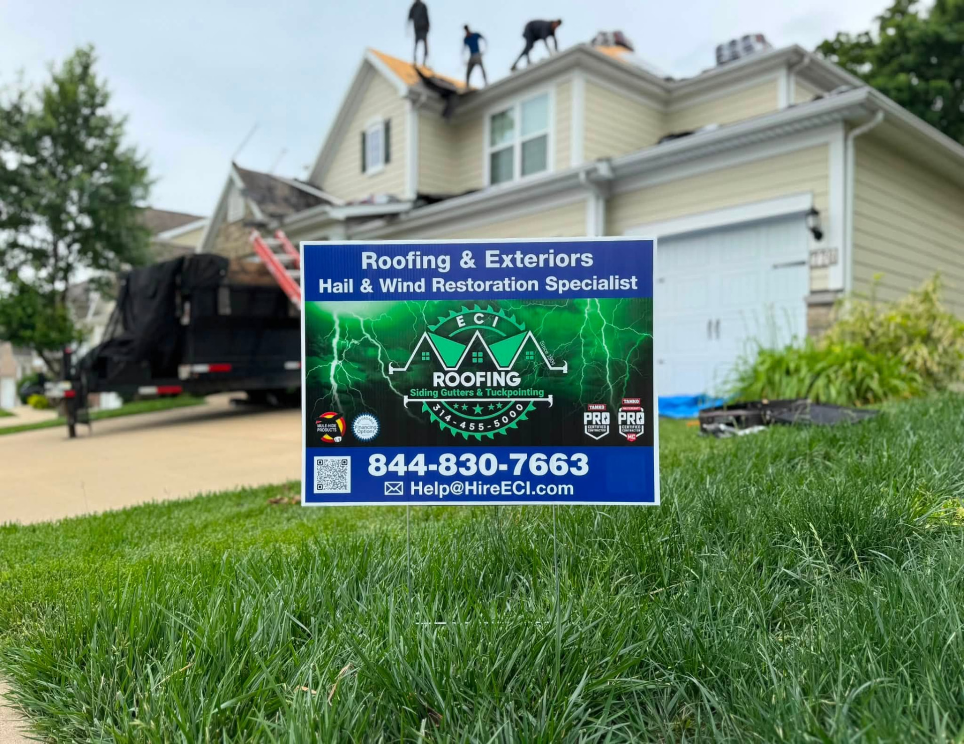 ECI yard sign in a front yard with the crew working on the roof behind
